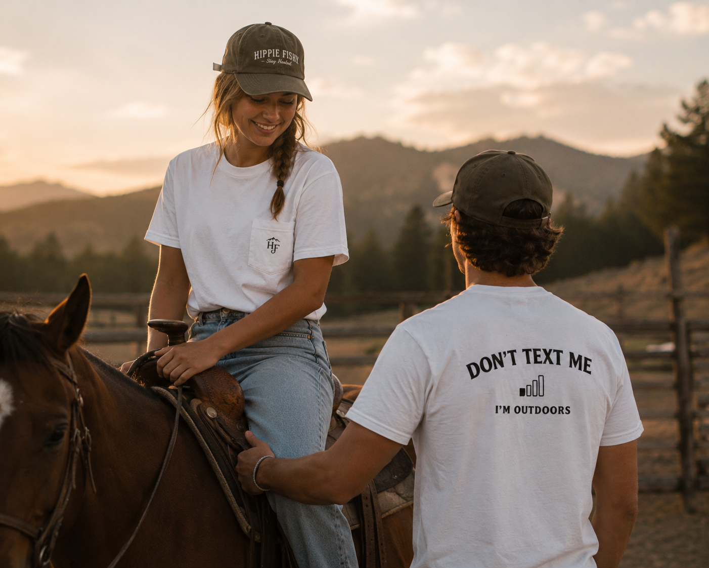 Two people wearing white "Don't Text Me I'm Outdoors" outdoor pocket tees in a ranch setting with a horse, designed for outdoor lifestyle and adventure.